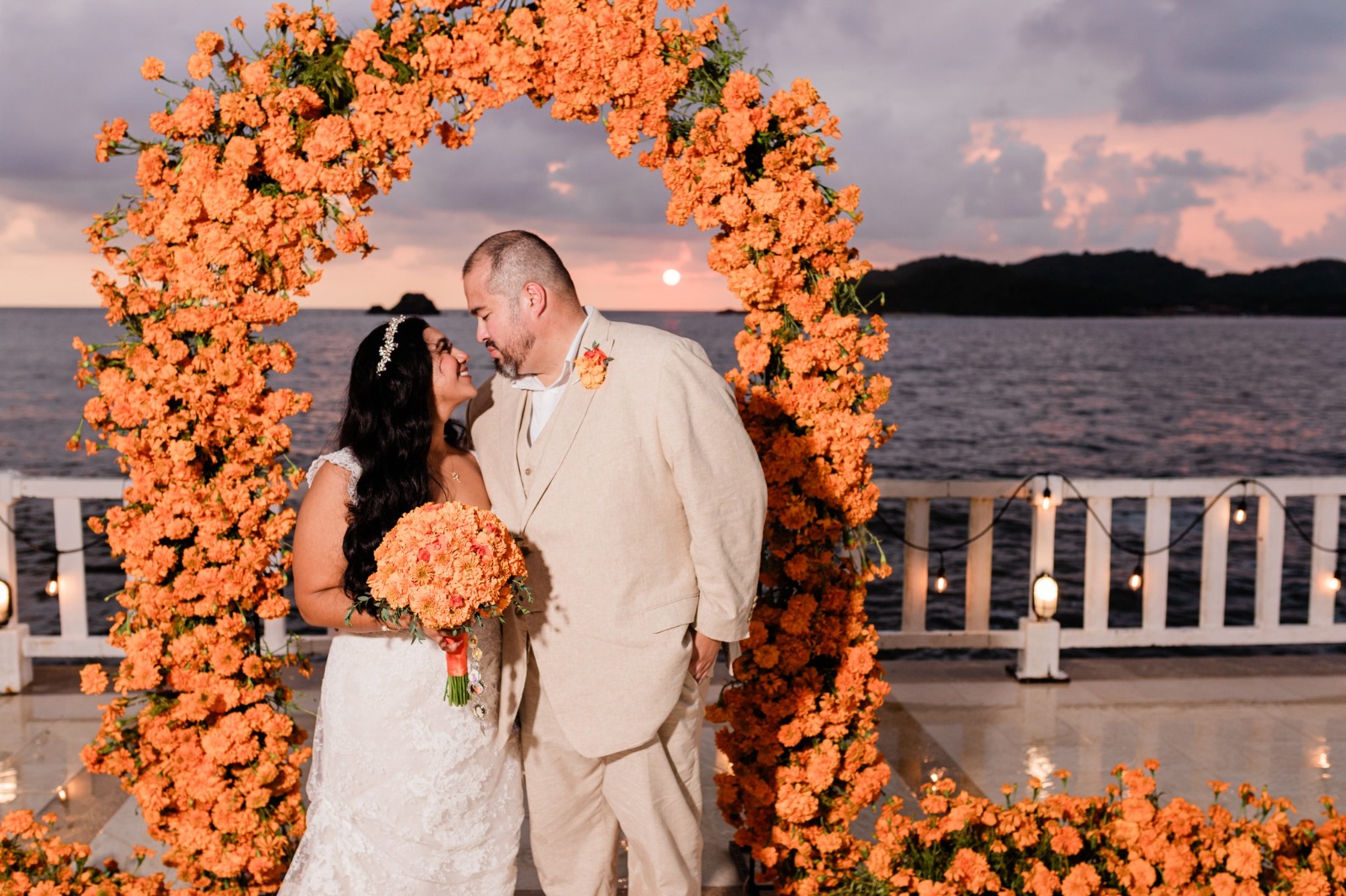 Julia y Byron frente a un arco floral en su boda